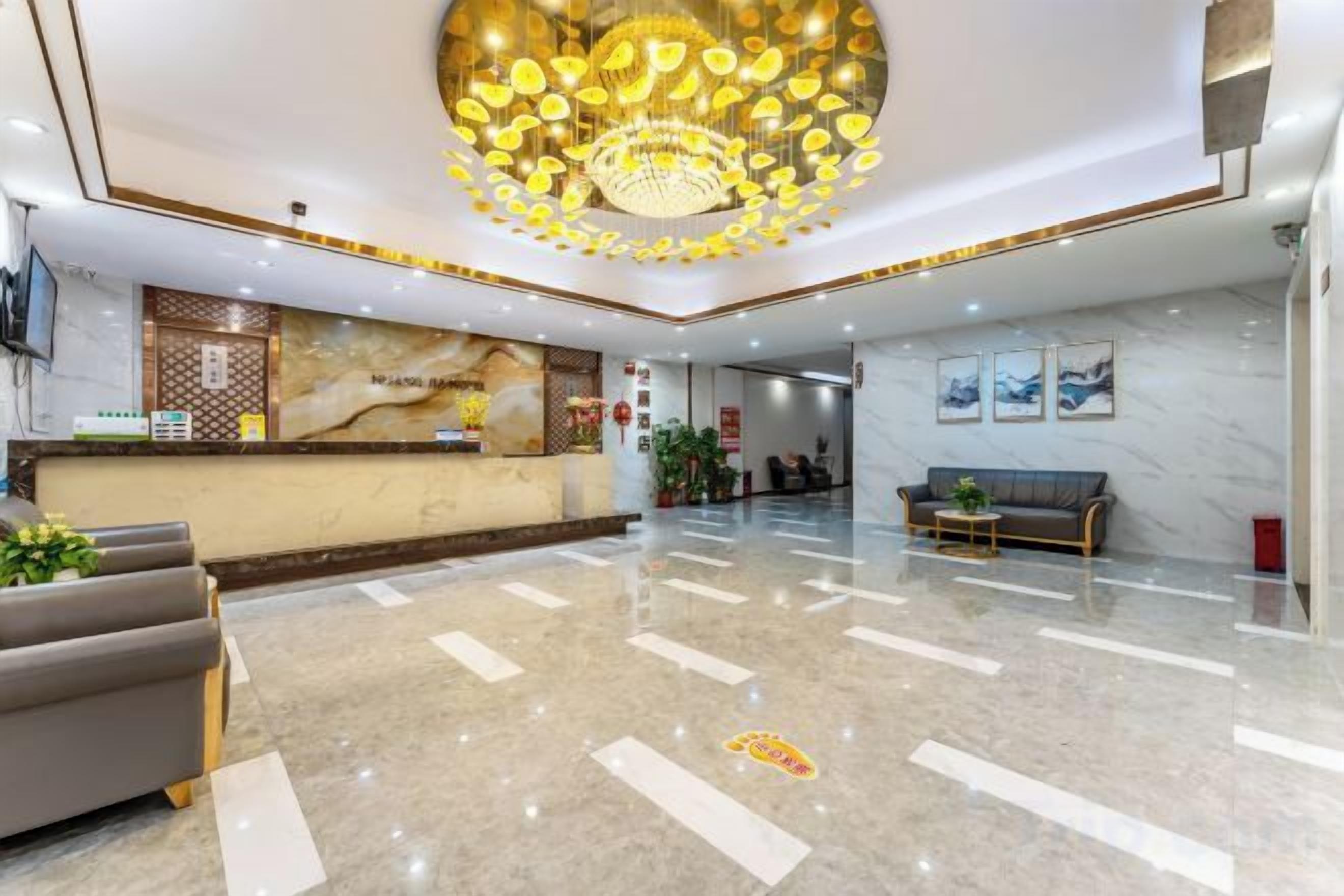 A hotel lobby with a reception desk, seating area, and a chandelier.