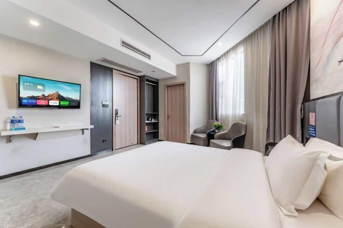 Et moderne hotelværelse med en stor seng, et fladskærms-tv monteret på væggen, et skrivebord med stol og et garderobeskab.