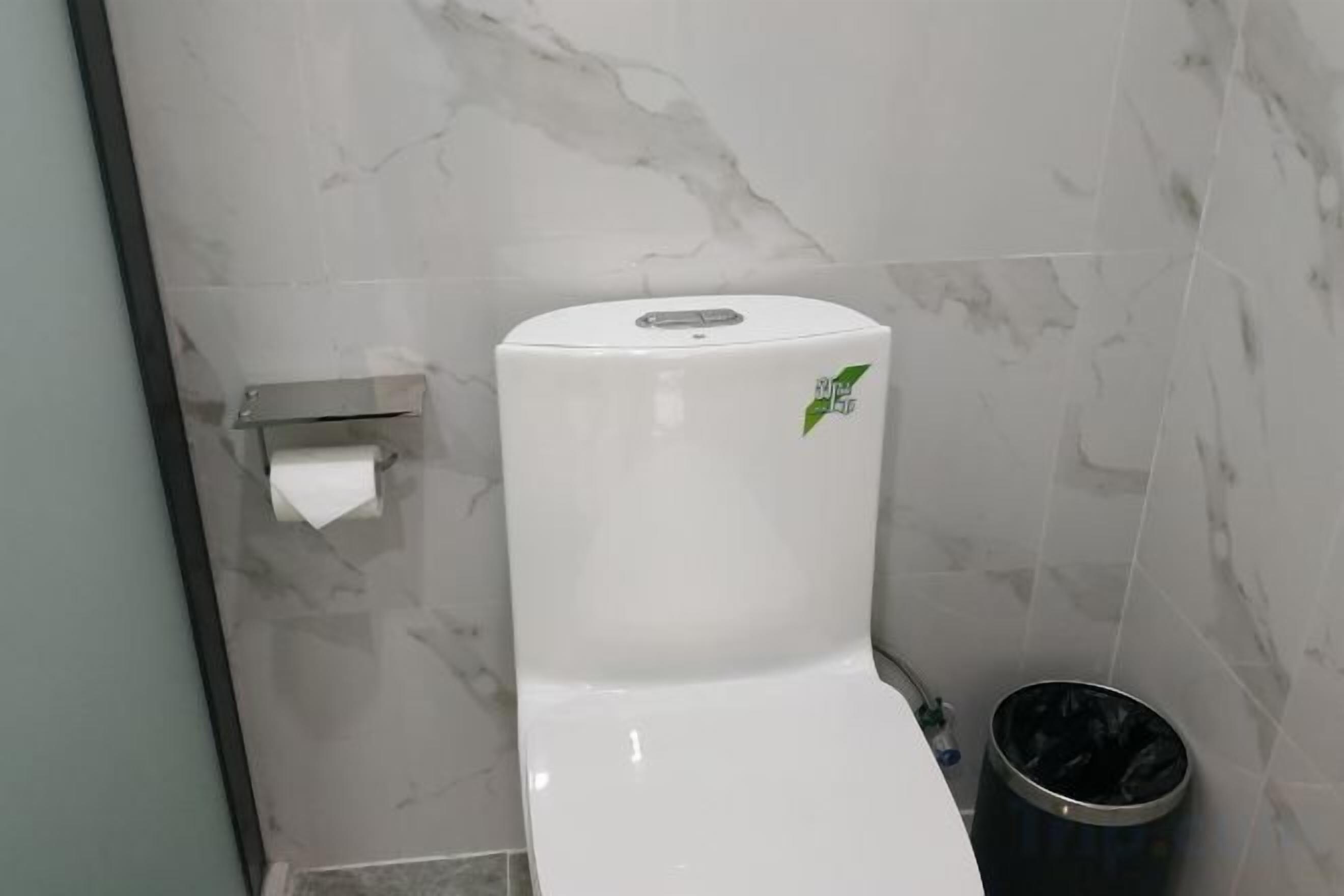 A toilet with a marble wall background and a trash bin.
