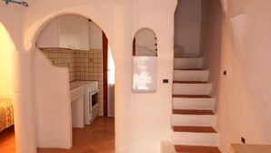 Ein schmaler Flur mit einer Treppe zum Obergeschoss, einer Küchenzeile mit gefliesten Wänden und einem gefliesten Boden.