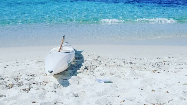 Ein Boot an einem sandigen Strand mit klarem, blauem Wasser und Horizont.