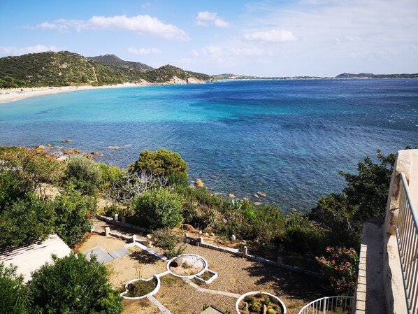 Blick auf die Küste mit Strand, klarem, blauem Meer und einer angelegten Gartenanlage mit Wegen und Grünflächen.