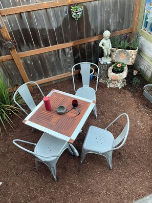 A patio with a wooden table and four gray chairs, surrounded by mulch and a wooden fence. - Book one week or more and get 10% discount
Stylish 2 BR Suite in West Seattle!
 (Seattle)