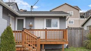 A two-story house with a wooden deck, a front door, and a small front yard with a tree and a fence. - Book one week or more and get 10% discount
Stylish 2 BR Suite in West Seattle!
 (Seattle)