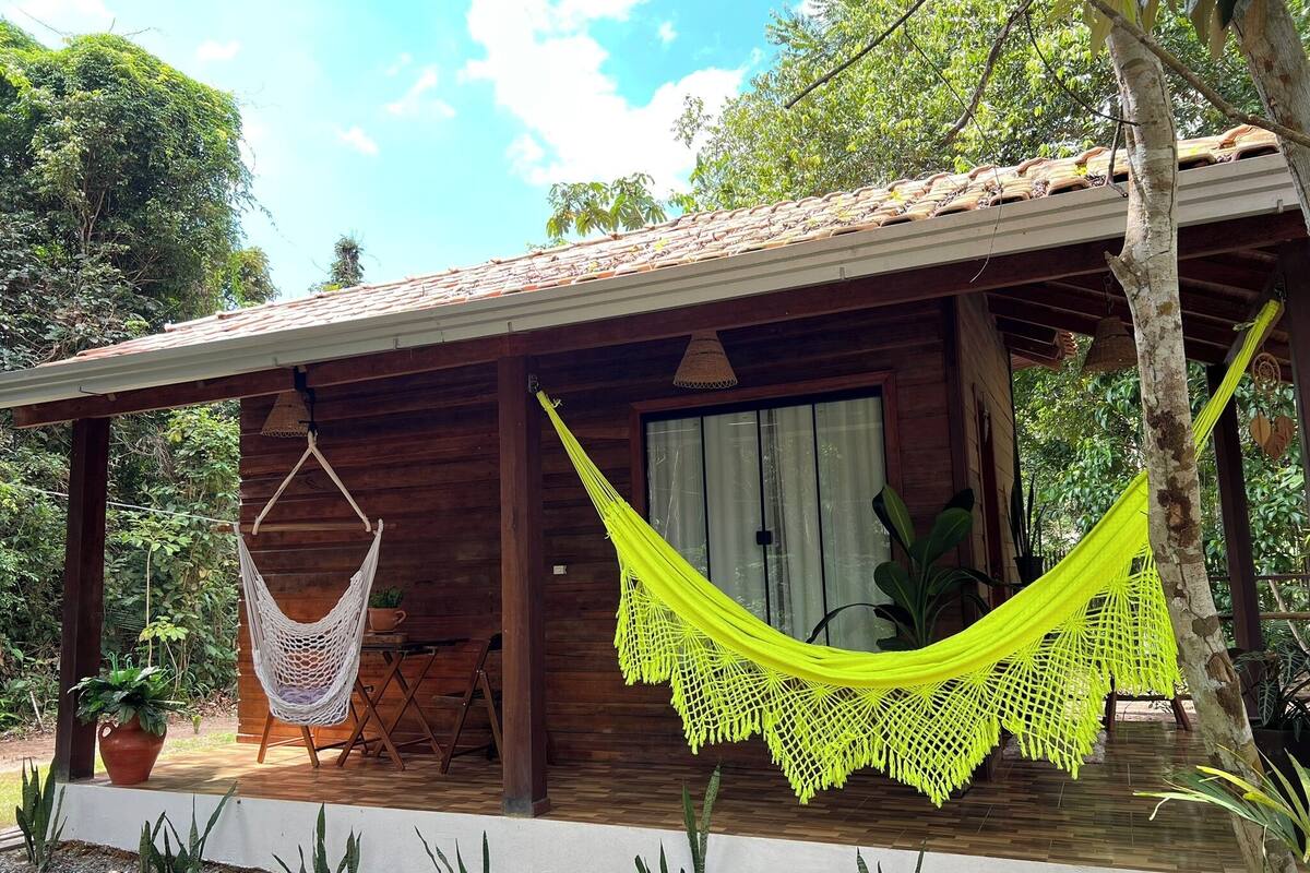 Una cabaña de madera con un porche, una hamaca y una planta en maceta.