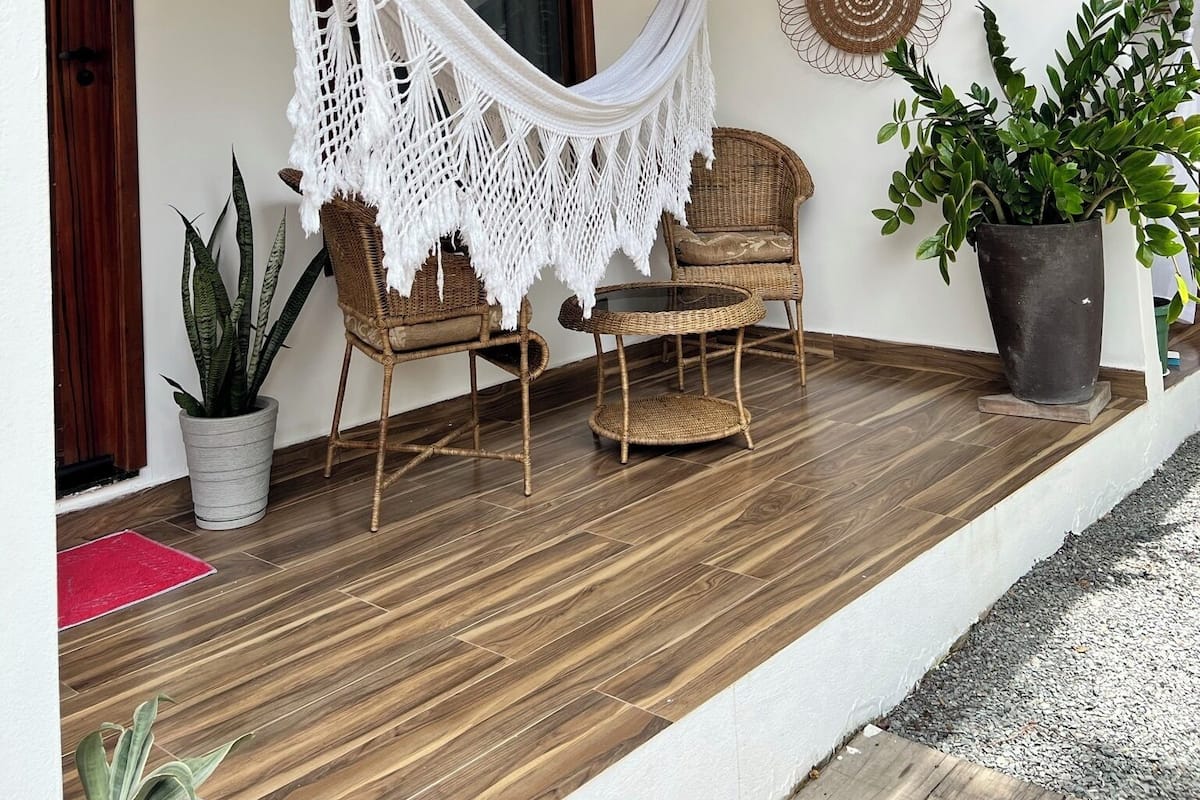 Un porche con una hamaca, muebles de mimbre, plantas en macetas y un ventilador de techo.