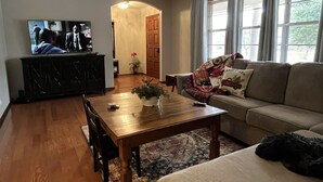 Un salon avec une table basse en bois, un canapé, un téléviseur posé sur un meuble noir et une porte donnant sur une autre pièce.