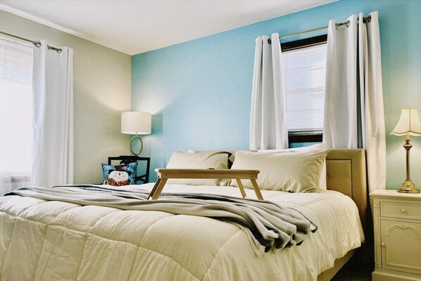 A neatly made bed with a wooden tray, a bedside lamp, and a nightstand with a lamp.