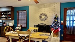 Un coin repas avec une cheminée en briques, un sapin de Noël et une table à manger en bois, accompagnée de chaises.