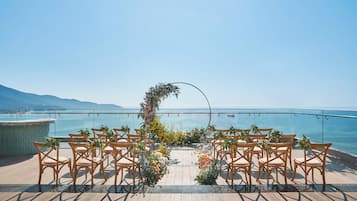 A wedding ceremony setup with chairs arranged in a semi-circle, a floral arch, and a view of the sea.