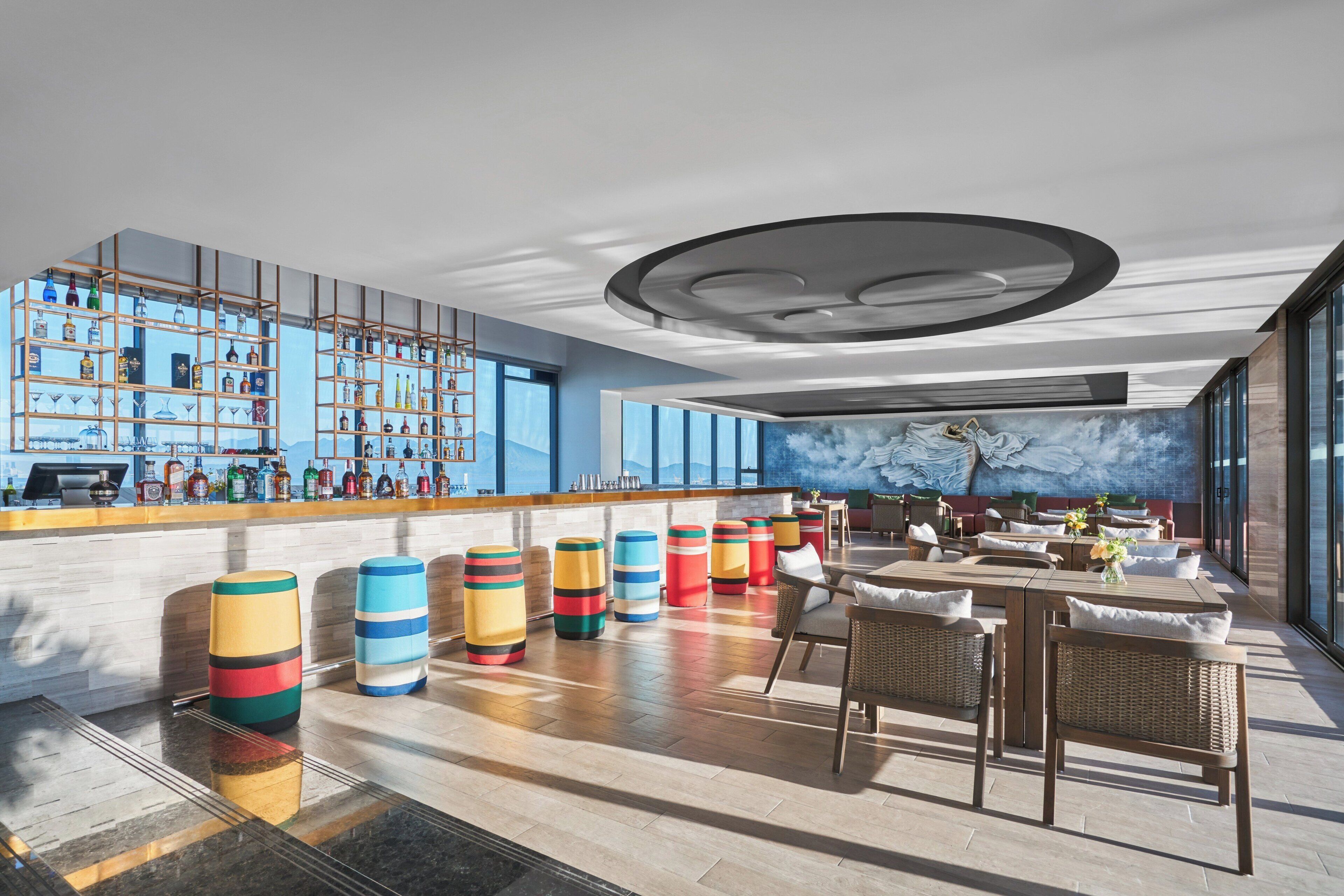 A modern bar area with a high bar counter, shelves of liquor bottles, and colorful stools.