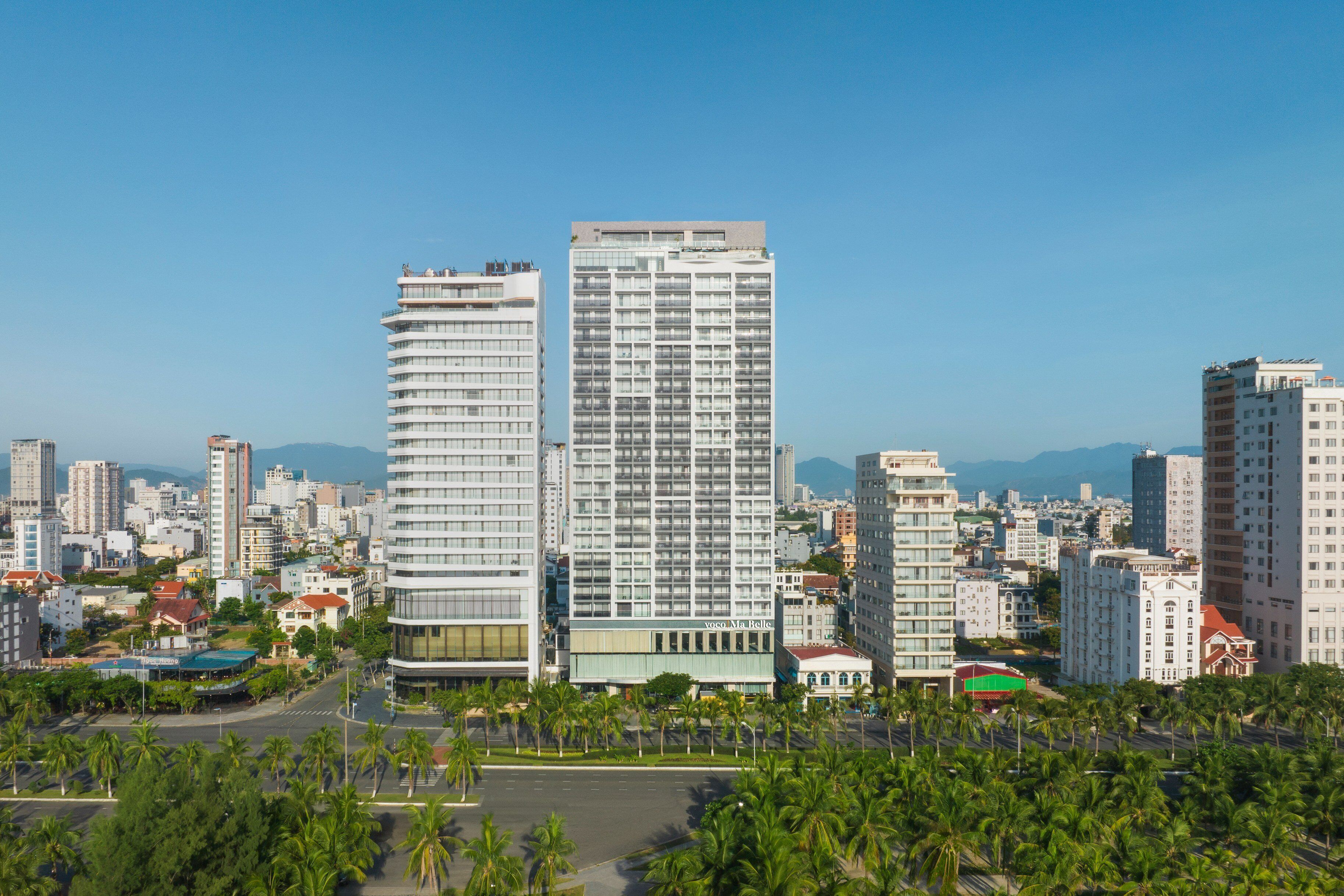 A modern high-rise hotel with a glass facade, surrounded by other buildings and palm trees.