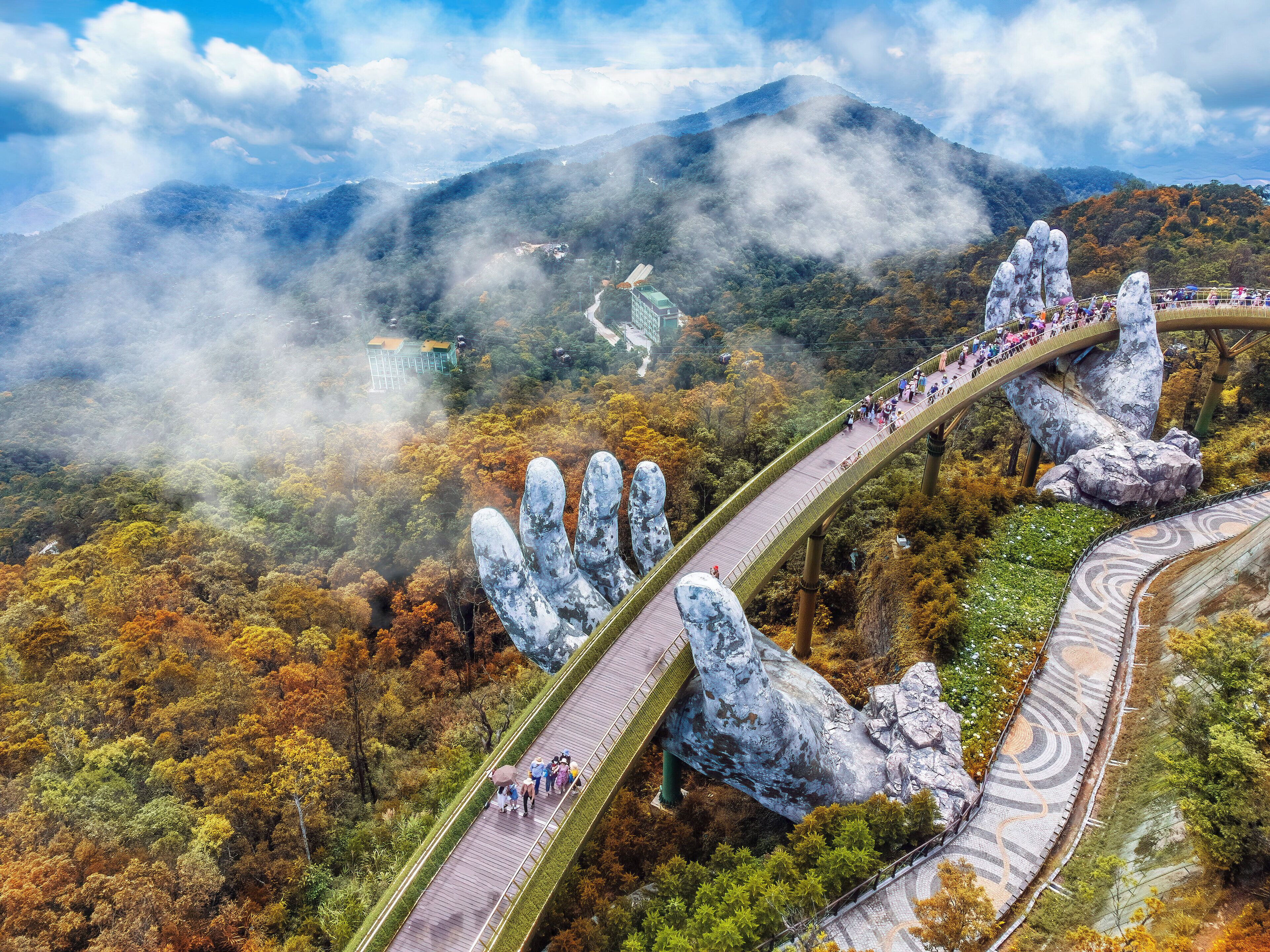 Un puente con un diseño único en forma de mano, rodeado de un paisaje boscoso con montañas al fondo.