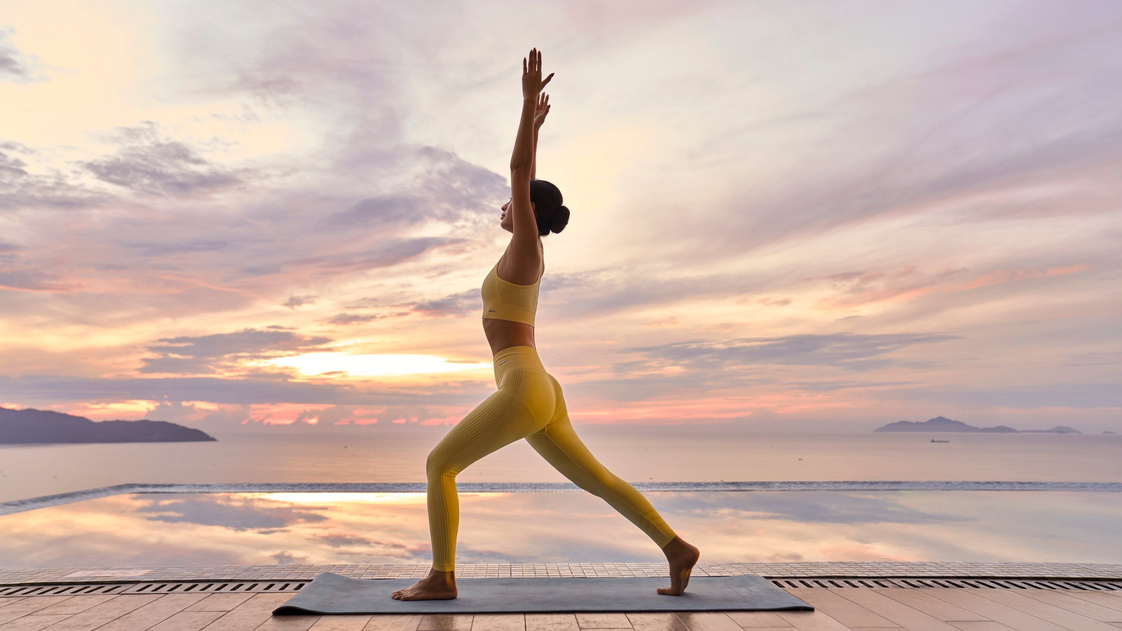A person performing a yoga pose on a mat with a scenic view of the ocean and mountains in the background.
