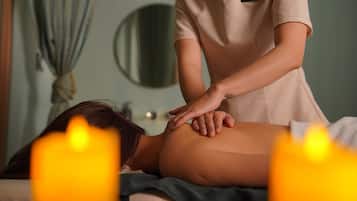 A massage therapy session in a room with a bed, a mirror, and candles.