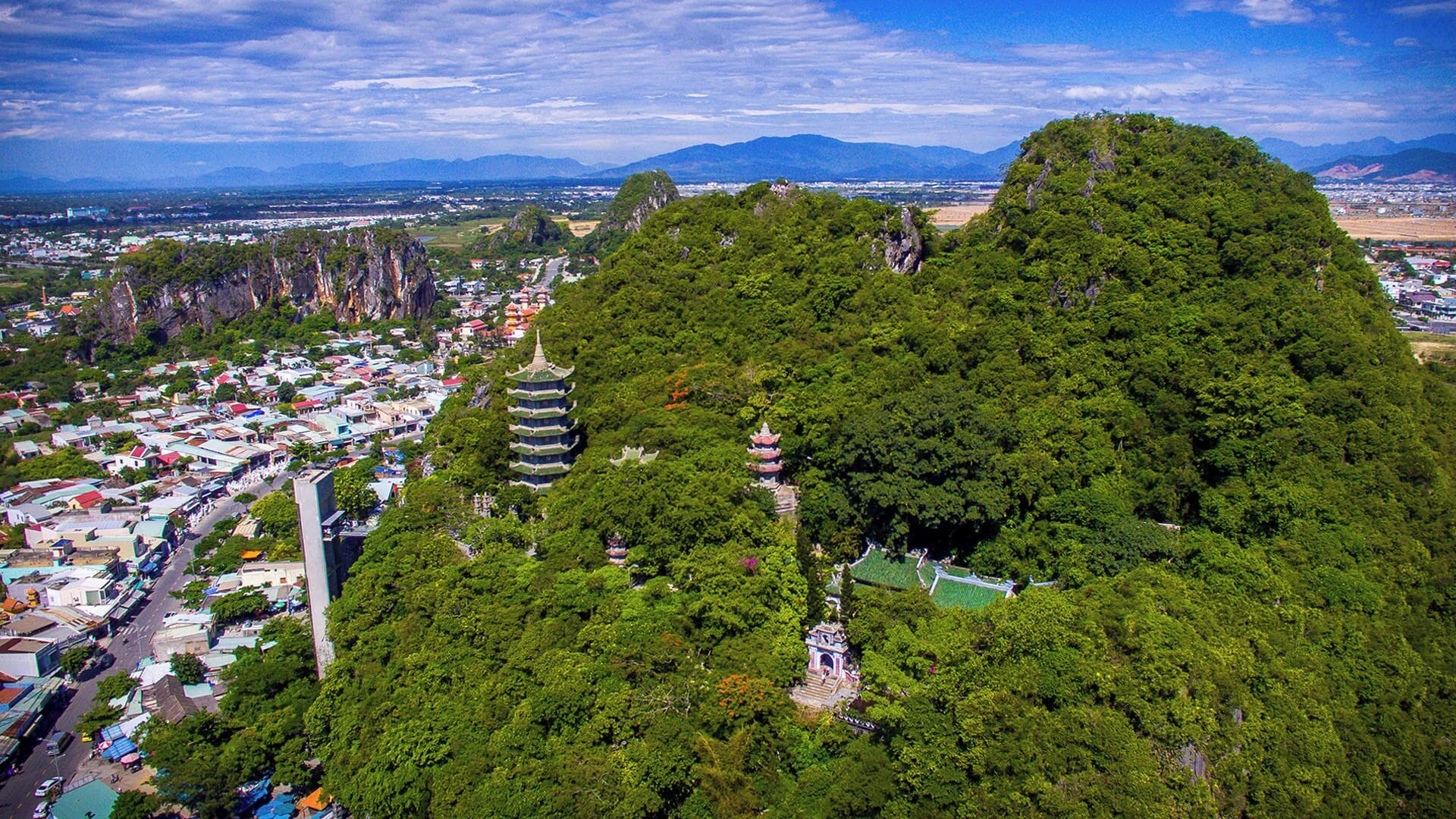 An aerial view of a mountainous area with a pagoda-style building surrounded by dense forest.