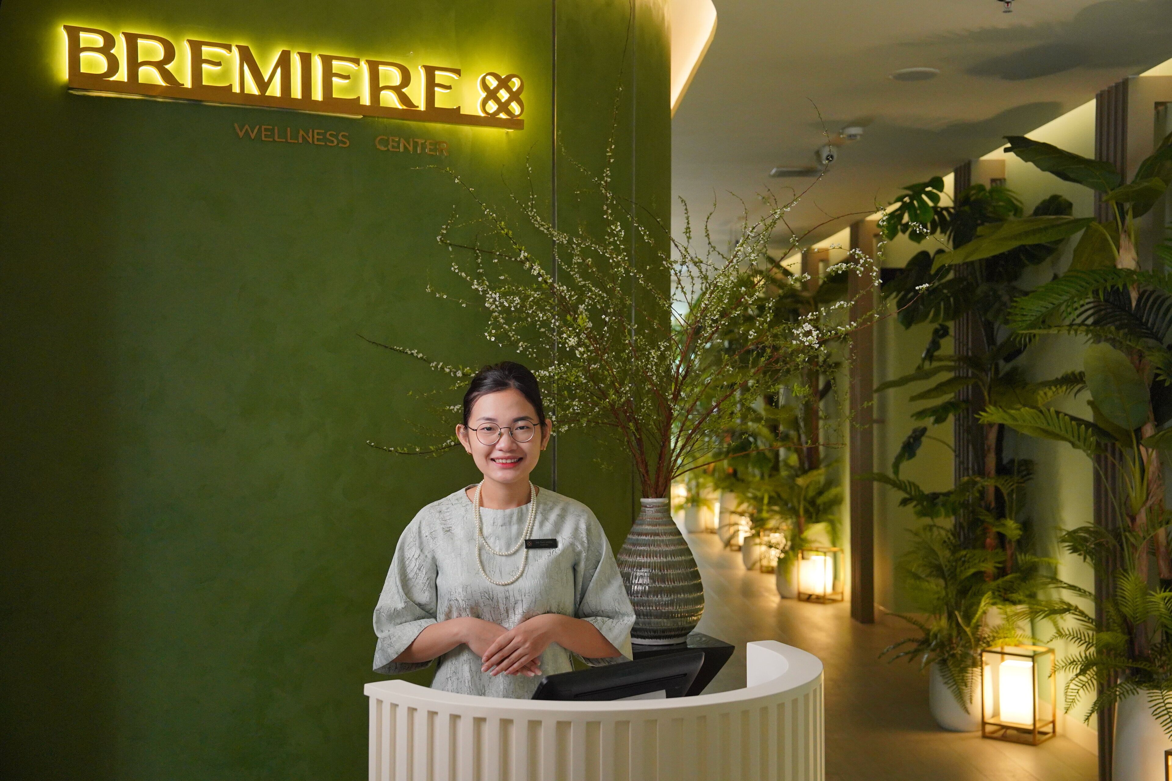A reception area with a sign reading "BREMIE Wellness Center" and a receptionist. There are potted plants and a vase with flowers.