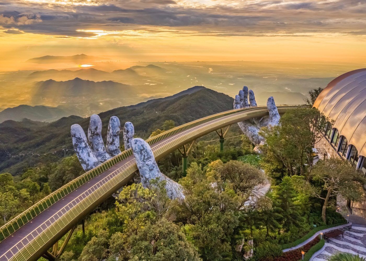 A bridge with a unique hand-shaped design, surrounded by lush greenery and mountains.