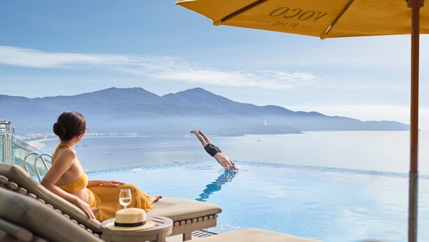 A person diving into a pool from a balcony overlooking a body of water and mountains. - voco Ma Belle Danang by IHG (Da Nang)