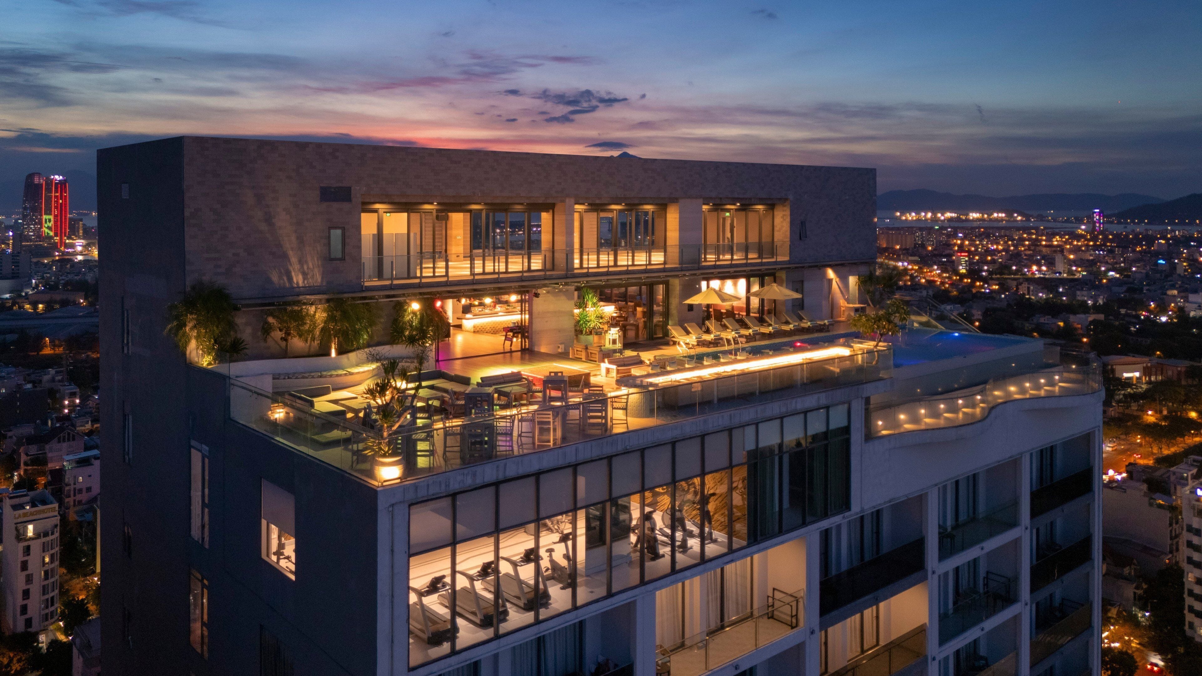 Un hotel modern amb bar a la terrassa, seients a l'aire lliure i una piscina.