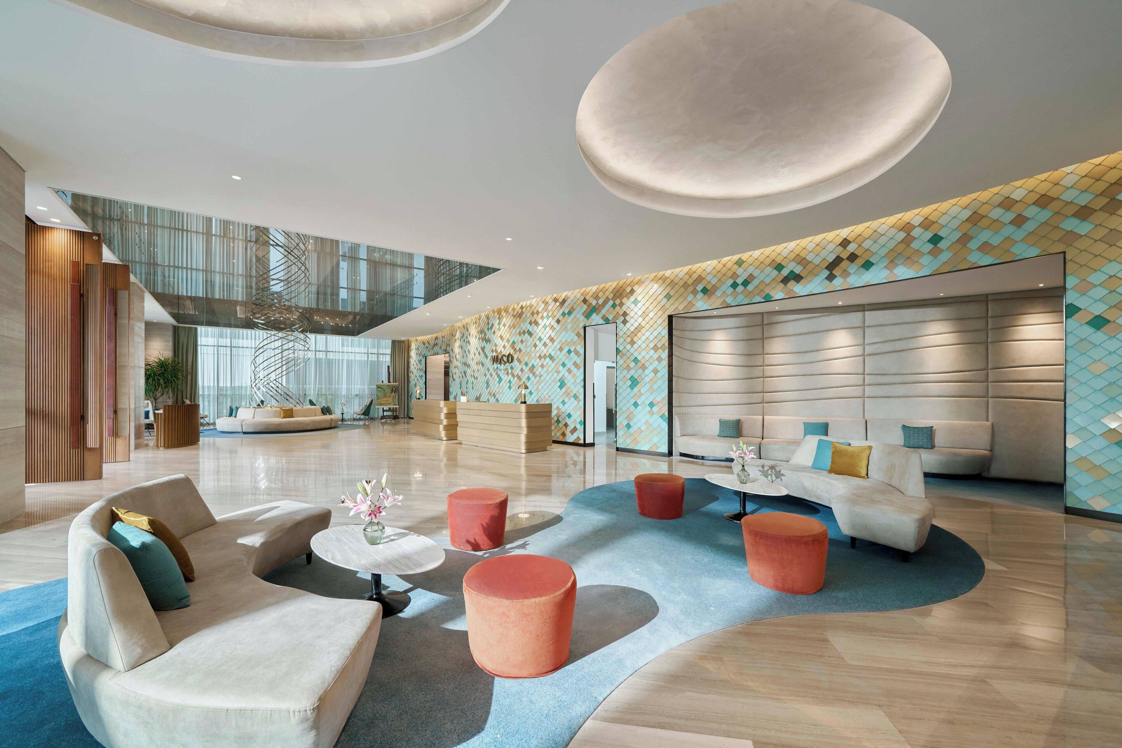 A spacious lobby with modern furnishings, a high ceiling, and a geometric patterned wall.