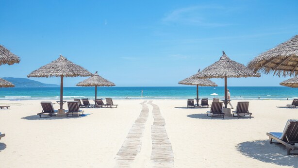 Una playa con tumbonas y sombrillas de paja.