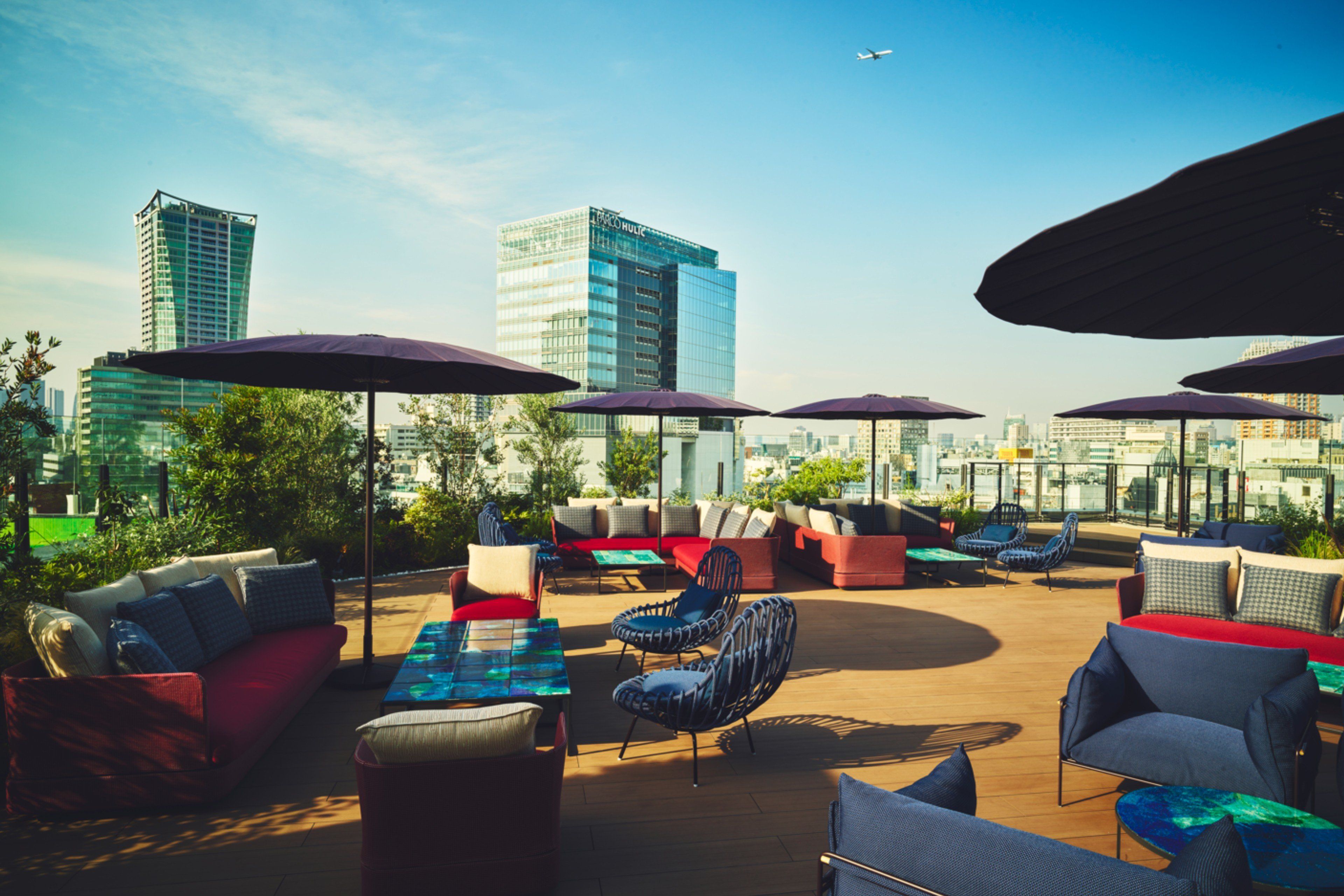 An outdoor seating area with multiple chairs and couches, umbrellas, and a view of the city skyline.