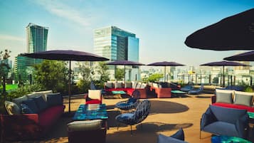 An outdoor seating area with multiple chairs and couches, umbrellas, and a view of the city skyline.