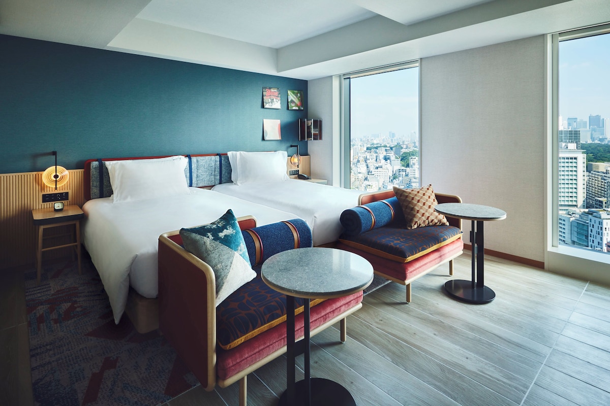 A modern hotel room with a large bed, two sofas, a small table, and a city view.