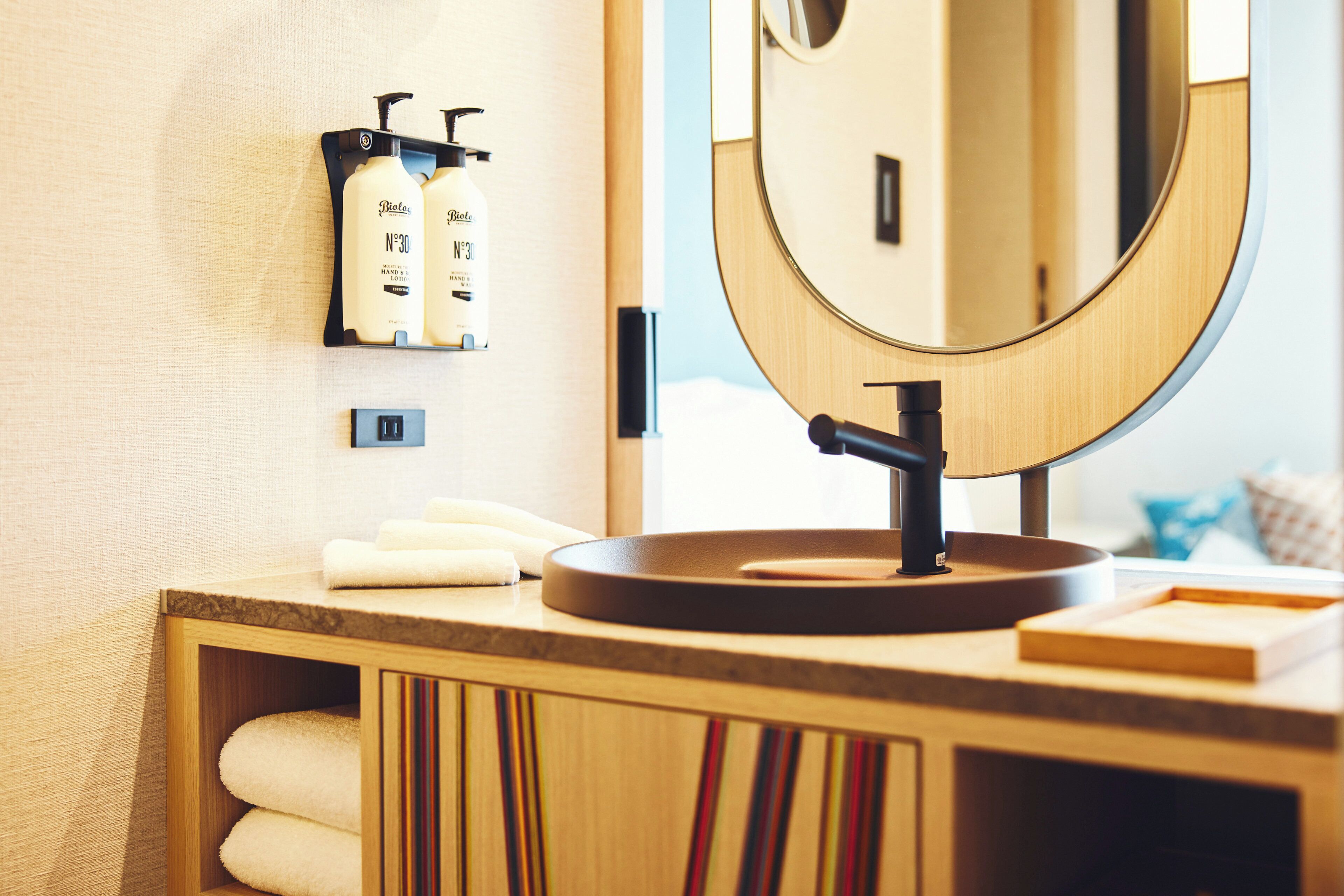 Un meuble-lavabo de salle de bain avec un miroir rond, deux distributeurs de savon liquide et un porte-serviettes.