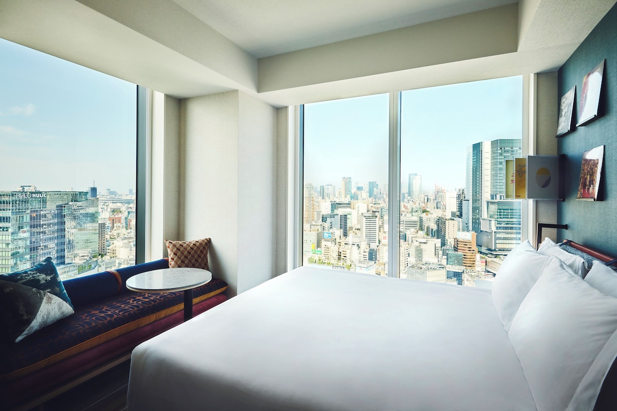 A hotel room with a large bed, a small round table, and a sofa with a city view.