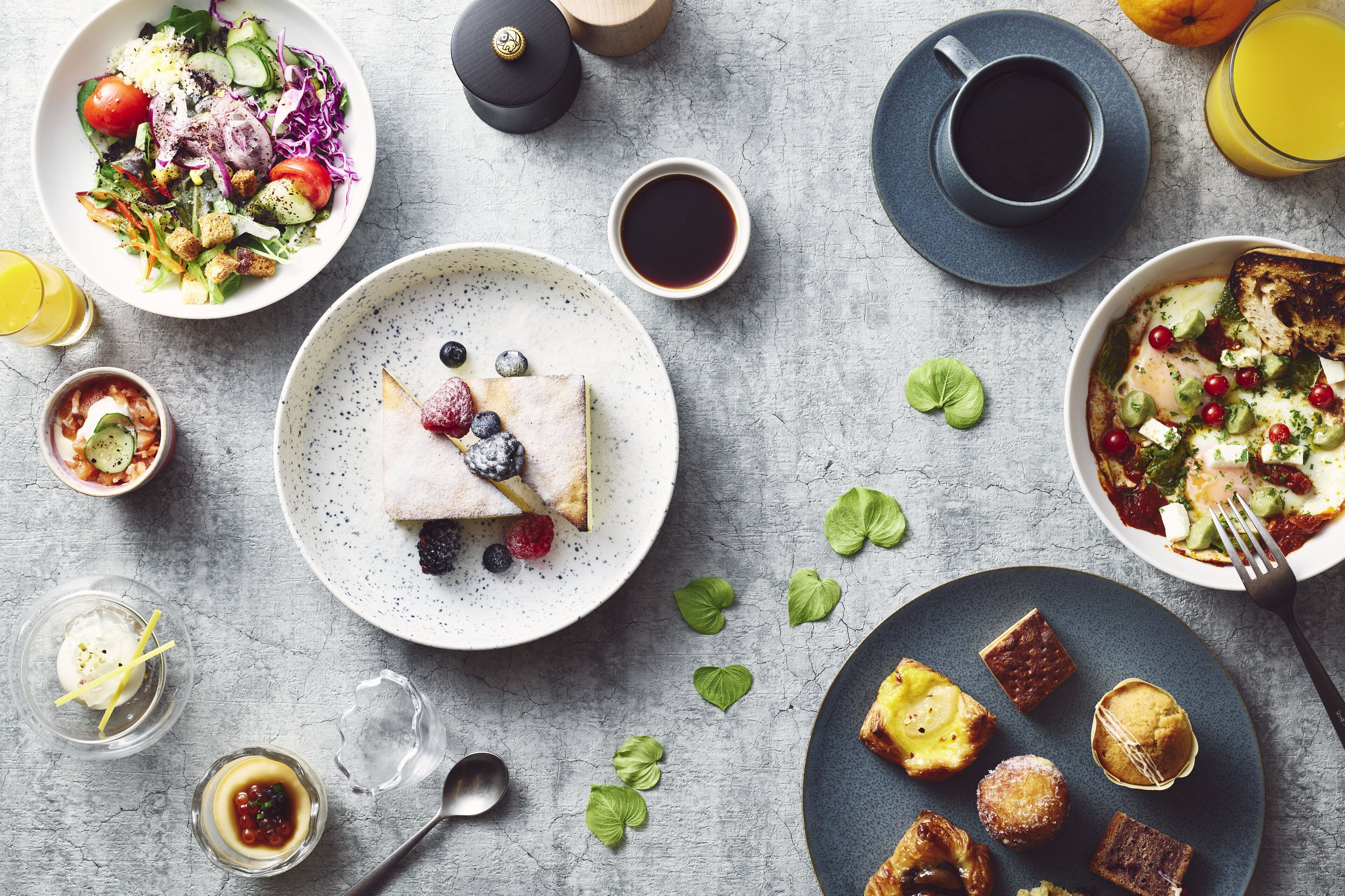 A breakfast setting with various dishes, including a salad, pancakes, and pastries, arranged on a table.