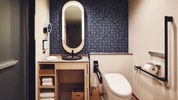 A compact bathroom with a toilet, a sink with a mirror, a towel rack, and a shelf with folded towels.
