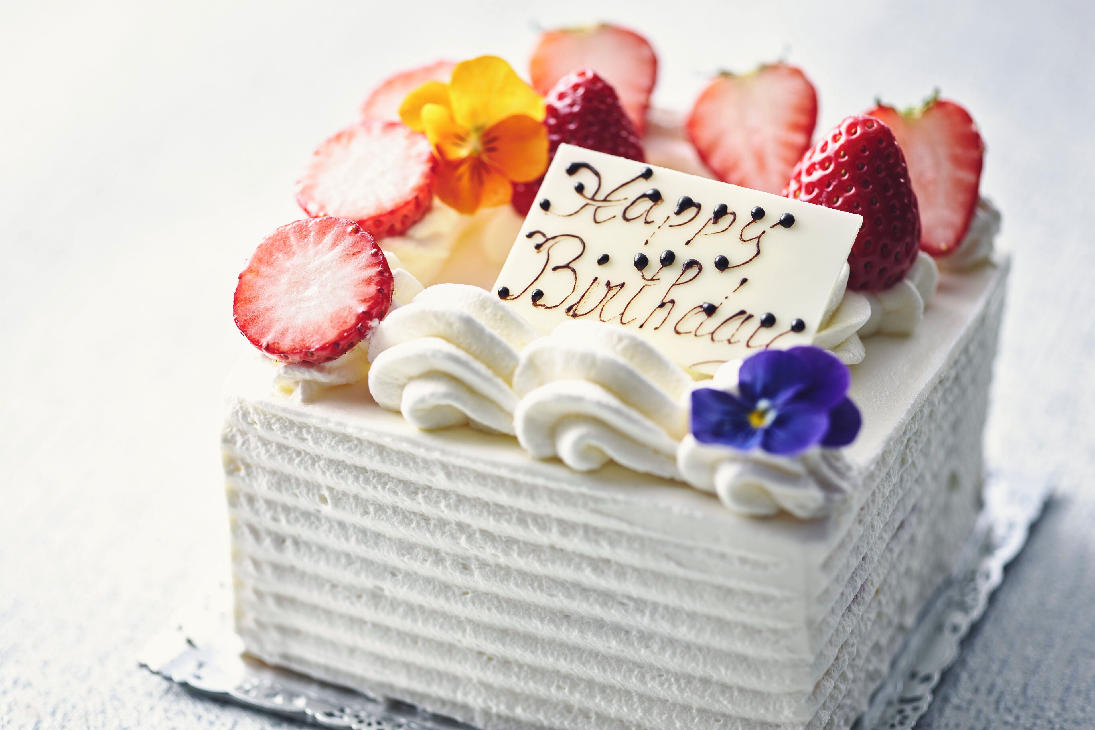 A birthday cake with a 'Happy Birthday' card, strawberries, and a flower on top.