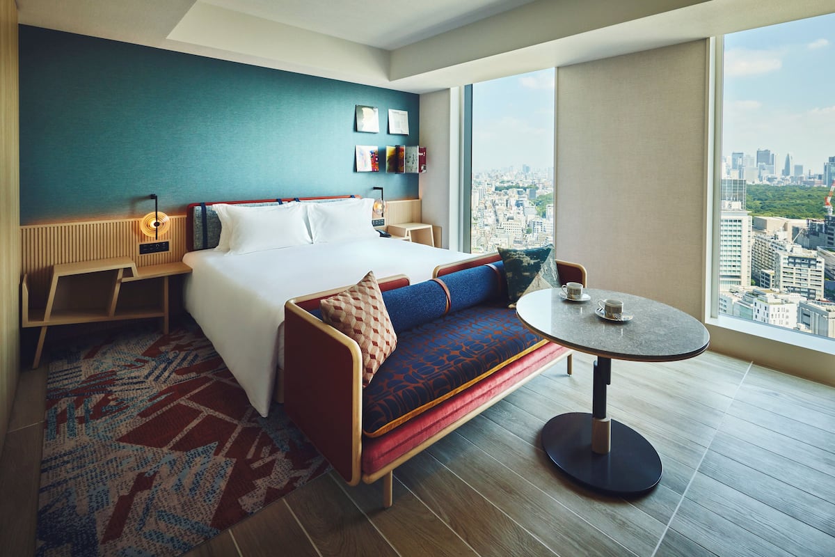 A modern hotel room with a large bed, a sofa, a small table, and a city view.
