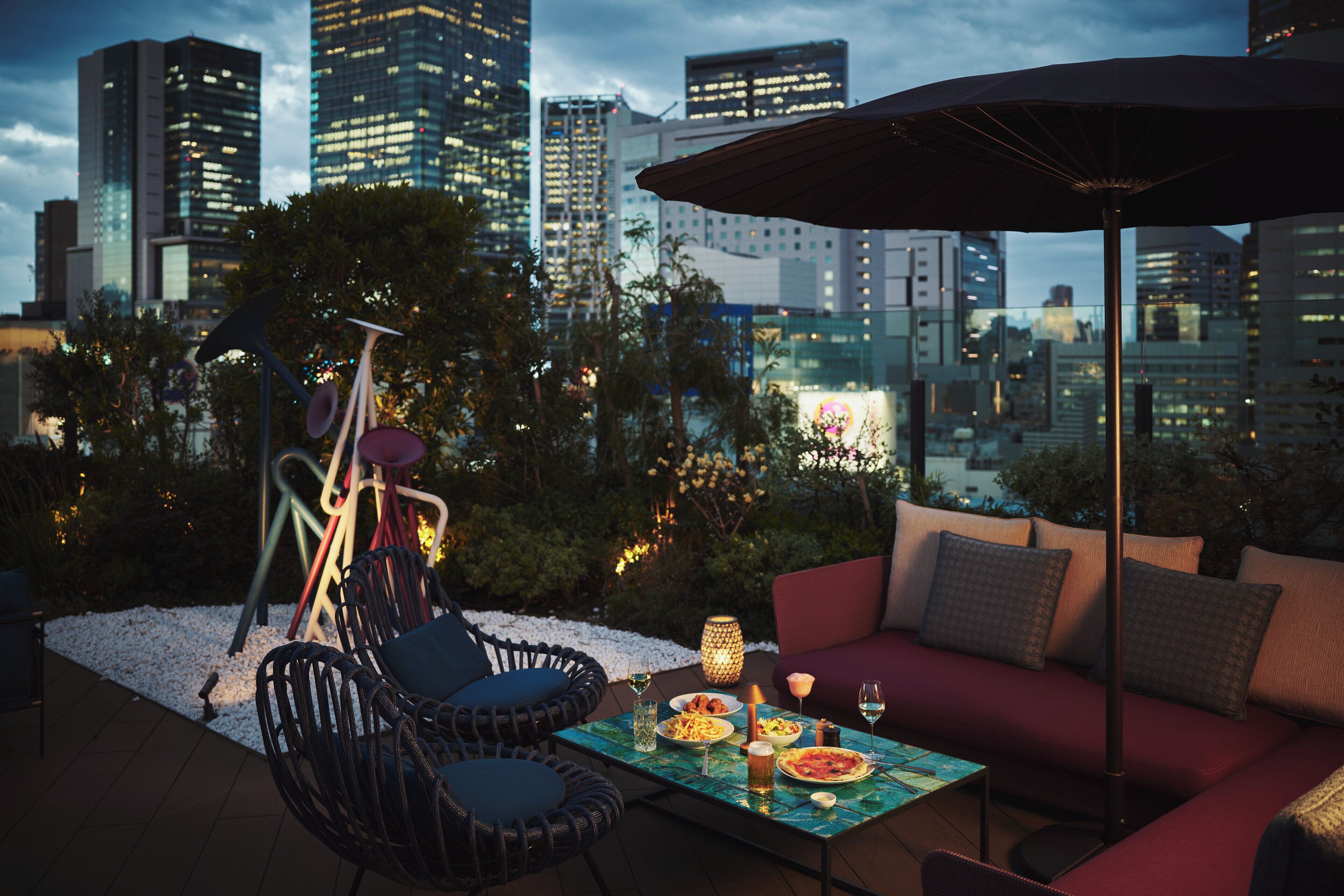 Una terraza en la azotea con mesa lista para comer, sillas, un sofá y una sombrilla.