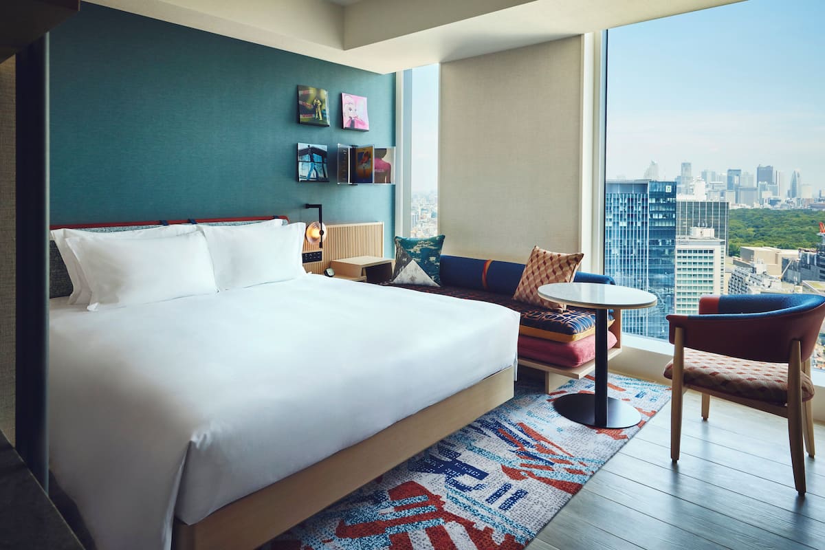 A hotel room with a large bed, a sofa, a small table, and a city view.