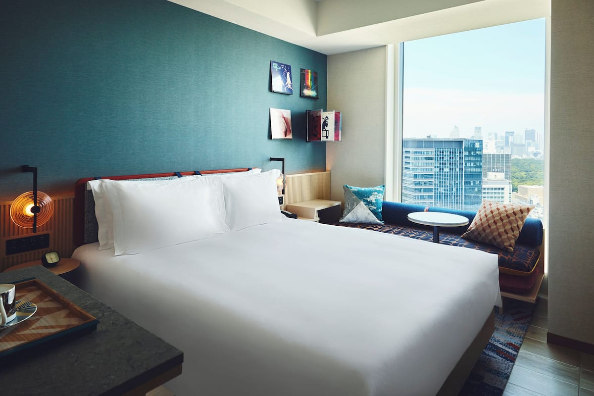A modern hotel room with a large bed, a seating area with a view of the city, and a small table with a tray.
