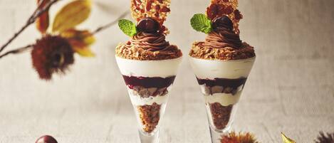 Two dessert cups with layered fillings and garnishes, placed on a textured surface with scattered fruits and leaves.