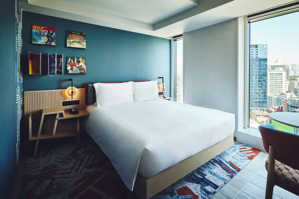 A modern hotel room with a large bed, a desk, and a city view.