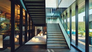 A modern interior with a staircase, glass walls, and a seating area with round lights.