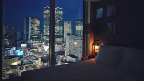 A hotel room with a large window offering a nighttime cityscape view.