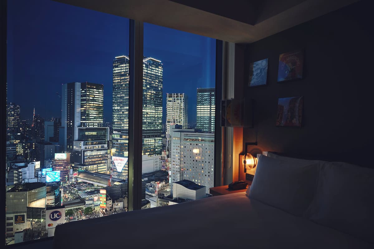 A hotel room with a large window offering a nighttime cityscape view.