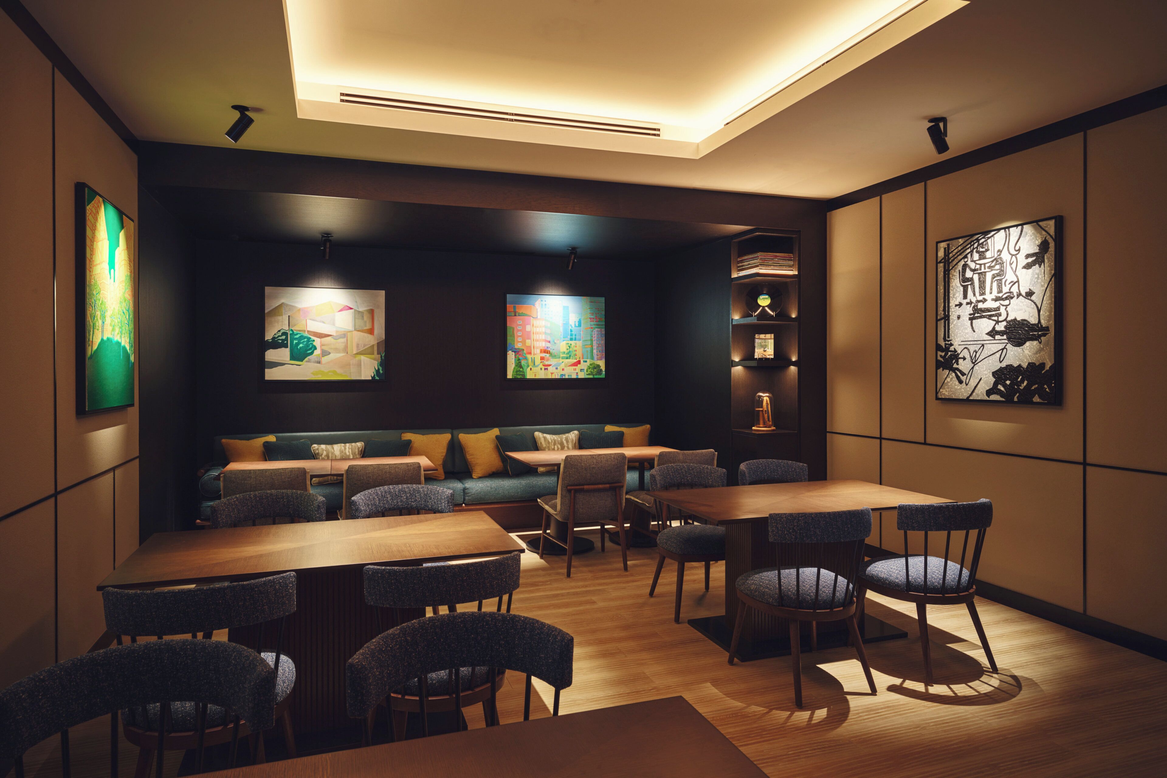 A modern dining area with wooden tables and chairs, a sofa, and artwork on the walls.