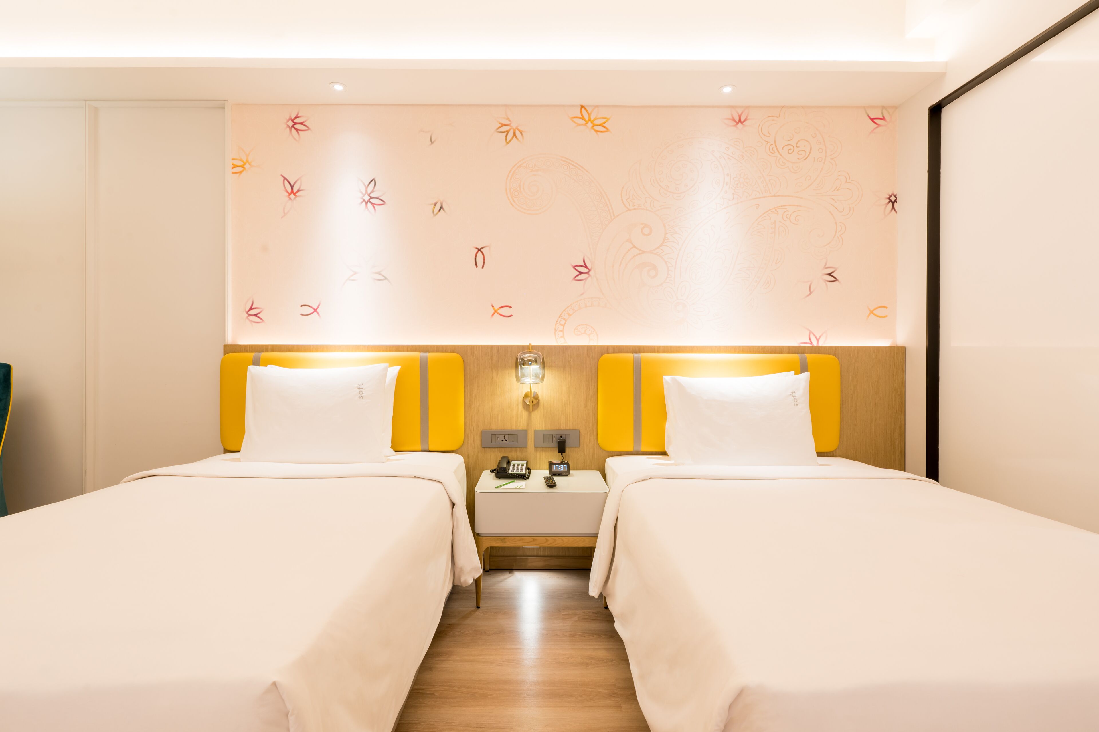 A hotel room with two beds, a nightstand with a phone and a lamp, and a decorative wall with floral patterns.