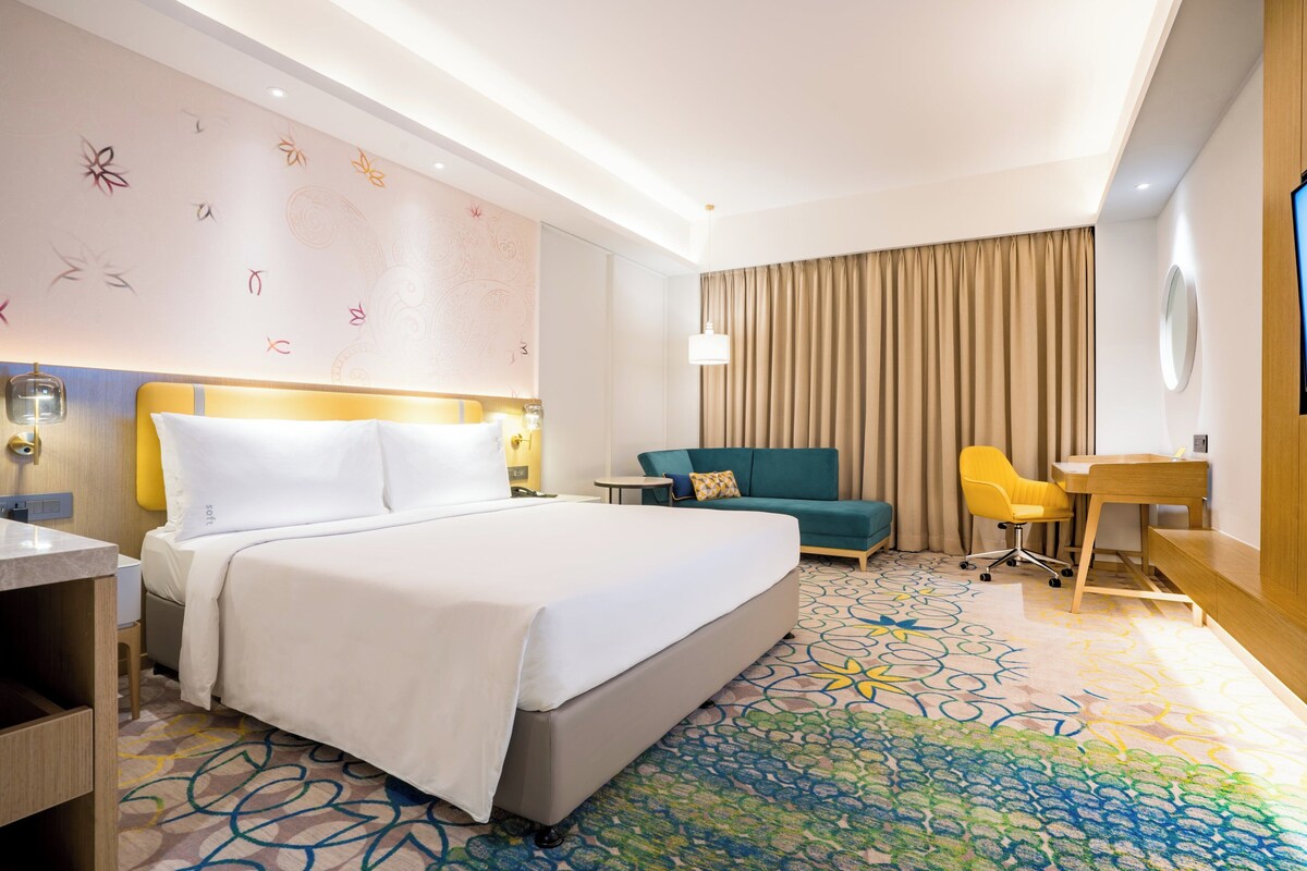 Een hotelkamer met een groot bed, een bureau, een stoel, een bank en een kamerbreed tapijt met een patroon.