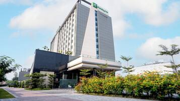 Un hotel Holiday Inn con un diseño moderno, que destaca por su entrada imponente y un área ajardinada con plantas florecientes.