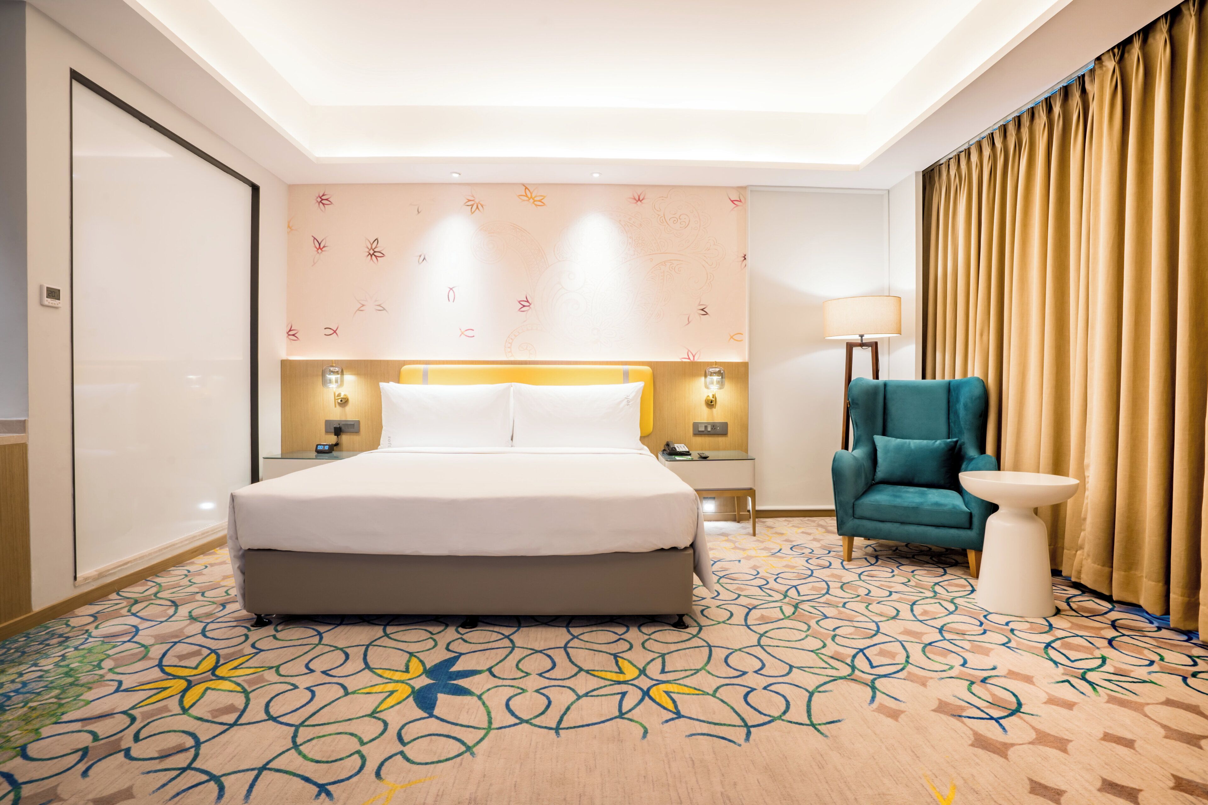 Una habitación de hotel con una cama grande, un escritorio, una silla, una lámpara y una alfombra estampada.