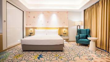 Una habitación de hotel con una cama grande, un escritorio, una silla, una lámpara y una alfombra estampada.