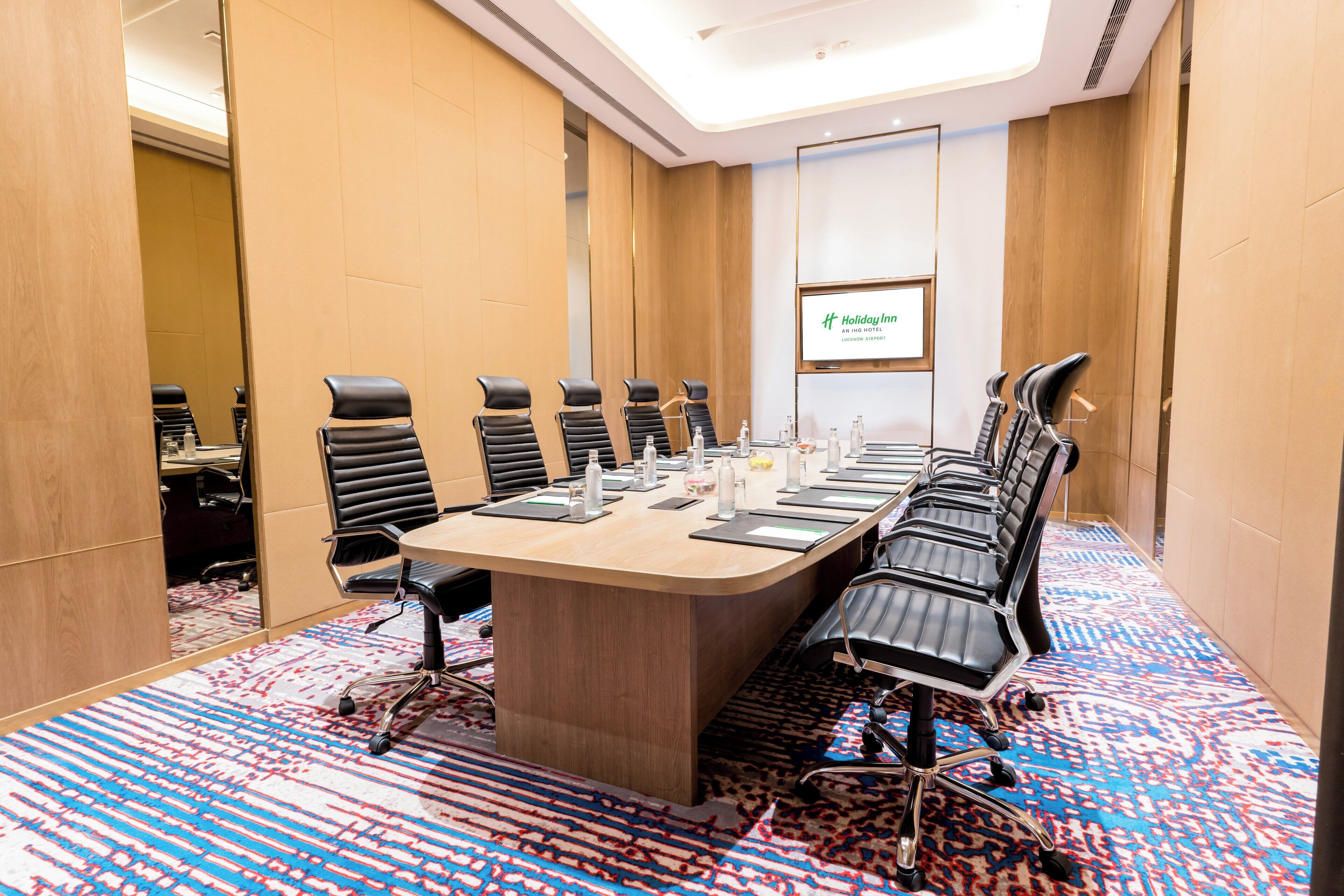 A conference room with a long table, multiple chairs, and a screen displaying the hotel name.